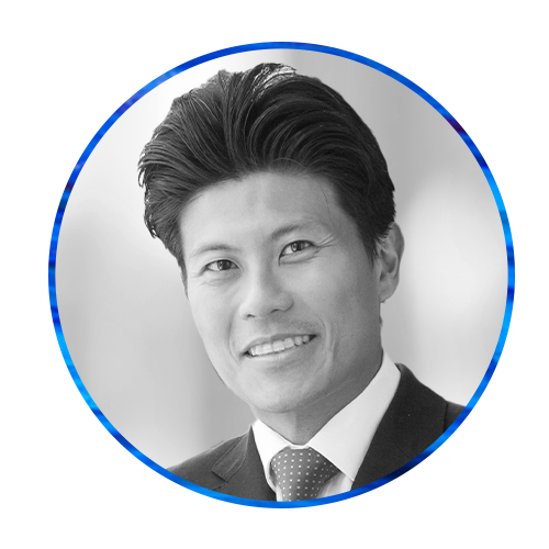 A person with dark, styled hair smiles while wearing a suit and tie. The background features a circular blue and white design, suggesting a professional or artistic atmosphere.