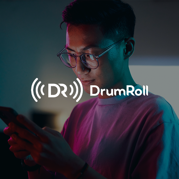 A young person wearing glasses is looking intently at their smartphone. The scene is illuminated by soft, colorful lighting in the background, suggesting a cozy indoor environment. The text "DR DrumRoll" is overlaid on the image.