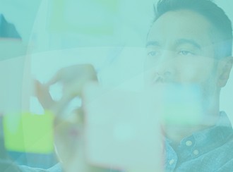 A man is focused on arranging colorful sticky notes on a transparent board, immersed in thought as he collaborates in a bright, modern workspace.