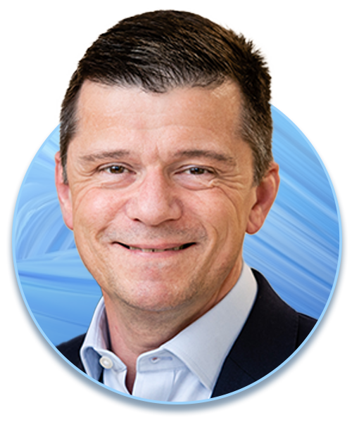 A man with short hair smiles, wearing a light blue shirt and dark blazer. The background features soft blue swirls, creating a professional and inviting atmosphere.