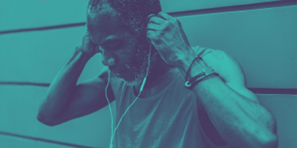An elderly man, wearing a tank top, adjusts his earphones while standing against a wall. The environment has a cool blue tint, creating a relaxed atmosphere.
