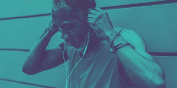 An elderly man, wearing a tank top, adjusts his earphones while standing against a wall. The environment has a cool blue tint, creating a relaxed atmosphere.