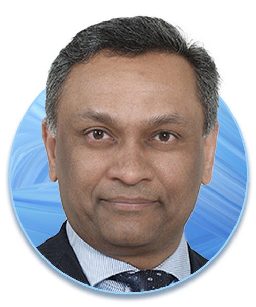 A man with short, dark hair and a slight smile is facing forward. He is wearing a dark suit and patterned tie, set against a circular blue background with textured waves.