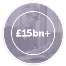 A woman wearing glasses is writing on paper. A circular overlay prominently displays “£15bn+” in bold letters. The background suggests a professional or office setting.