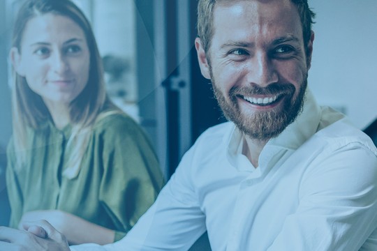 Three people are engaged in a conversation, smiling and looking at each other in a well-lit, modern office environment with soft blue hues and a minimalist aesthetic.