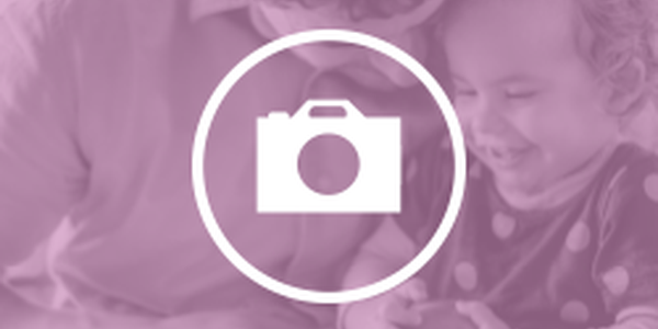 A smiling adult closely engages with a joyful child, sharing a moment of play or exploration, all set against a soft pink background.