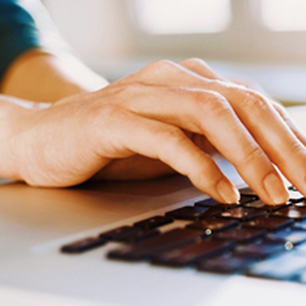 A hand is typing on a laptop keyboard. The setting appears to be a bright indoor space with soft natural light coming from nearby windows, creating a warm atmosphere.
