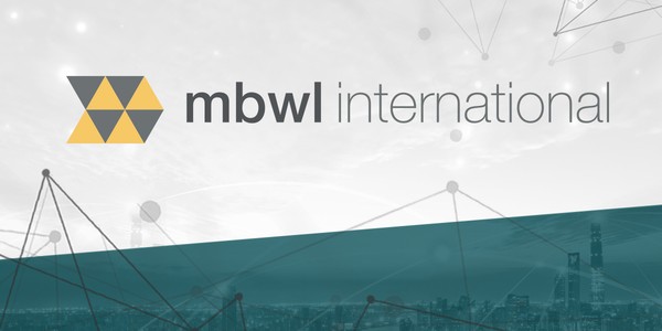 A geometric logo exhibits interlocking triangles in yellow and gray. The text "mbwl international" appears beside it, set against a blurred city skyline and a light-colored background conveying a modern, tech-oriented context.