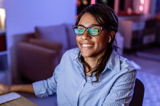 A smiling female with screen reflecting on glasses.