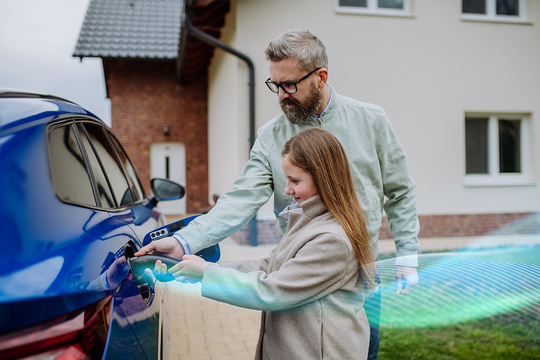 A girl and an adult man are standing outside, interacting with a blue electric vehicle. The girl holds a charging connector, while an animated glow suggests energy transfer in a residential setting.