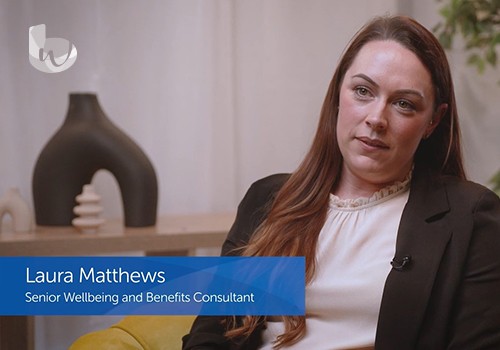 A woman with long brown hair sits in a chair, looking thoughtfully at the camera. A modern vase and a plant are visible in the background. Text reads: "Laura Matthews, Senior Wellbeing and Benefits Consultant."