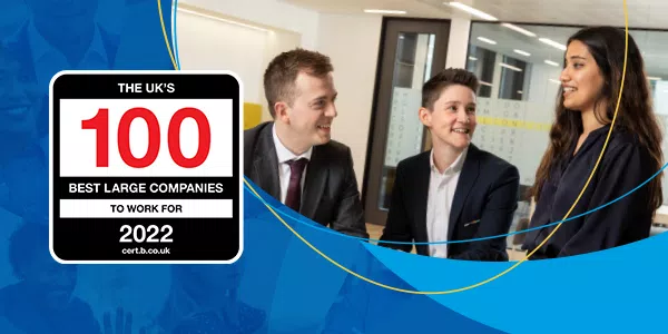 Three professionals gather in a modern office setting, engaging in conversation. A graphic prominently displays "THE UK's 100 BEST LARGE COMPANIES TO WORK FOR 2022" with the website cert.b.co.uk.
