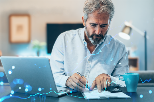 A middle-aged man is writing notes while seated at a desk with a laptop. He is focused, surrounded by a modern workspace, and a blue coffee cup is nearby. Graphical data overlays are visible.