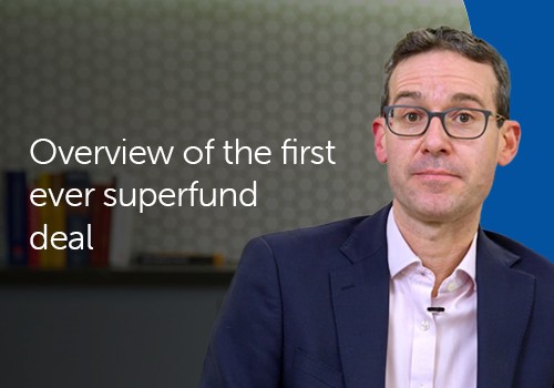 A man in a suit sits in front of a patterned background, speaking directly to the camera. Text next to him reads: "Overview of the first ever superfund deal."
