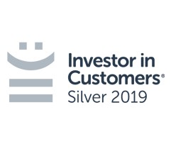 A logo featuring a smiley face above horizontal lines, accompanied by the text "Investor in Customers® Silver 2019," indicating recognition for customer investment and satisfaction.