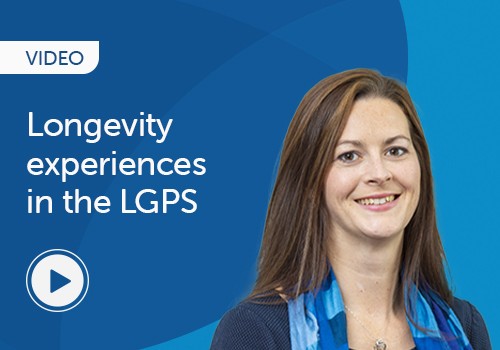 A woman with long brown hair is smiling while wearing a blue scarf over a blazer. She appears to be presenting or discussing a topic related to “Longevity experiences in the LGPS.” The background is a gradient of blue. A play button is visible, indicating