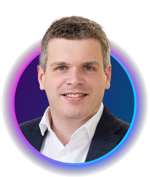 A man with short, light brown hair smiles confidently. He wears a dark blazer over a white shirt. The background features a circular, colorful gradient that enhances the portrait.