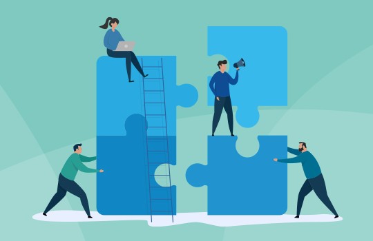 Four people interact with large puzzle pieces in a light green space. One person is on a ladder working on a piece, while another holds a megaphone. Two others are arranging pieces together.