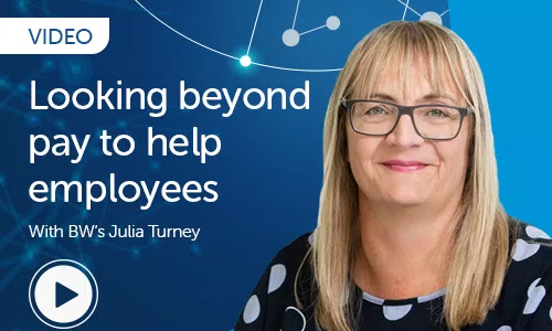 A woman with glasses and long hair is smiling. The context features a blue background with network-like graphics. Text reads: "VIDEO Looking beyond pay to help employees With BW's Julia Turney." A play button is present.