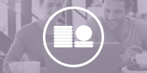 Two people smile while engaging with a laptop, likely discussing finances or planning. They are seated at a table, surrounded by coffee cups and fruit, in a casual indoor setting.