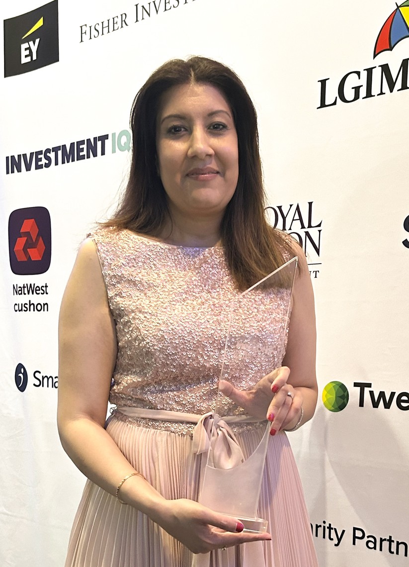 A woman in a sparkling pink dress holds a clear award against a backdrop of various corporate logos. She is smiling, suggesting a celebratory event.