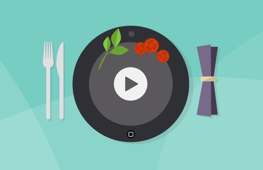 A black plate with fresh herbs and red tomatoes sits at the center. A play button symbol is displayed on the plate. Fork and knife are positioned on the left, while rolled napkins sit on the right, all against a light teal background.