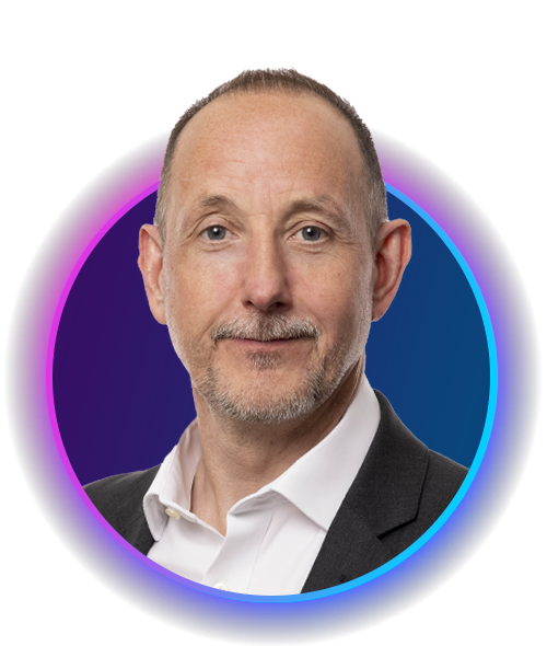 A man with short brown hair and a beard smiles, wearing a white shirt and black blazer. He is framed within a colorful circular design against a dark background.