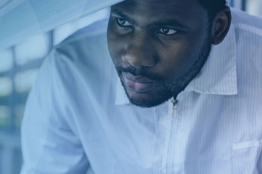 A man in a white shirt examines plants in a controlled environment, focused intently on his task while surrounded by rectangular light panels and greenery in the background.