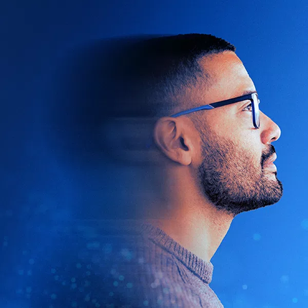 A man with glasses gazes thoughtfully to the right, set against a vibrant blue background with a soft, blurred effect, suggesting a contemplative or inspirational moment.