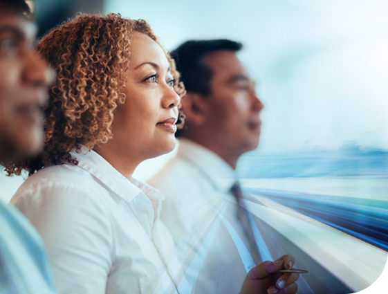 A woman with curly hair sits thoughtfully alongside two men, gazing forward as blurred motion suggests high-speed movement, conveying a sense of anticipation and focus in a dynamic environment.