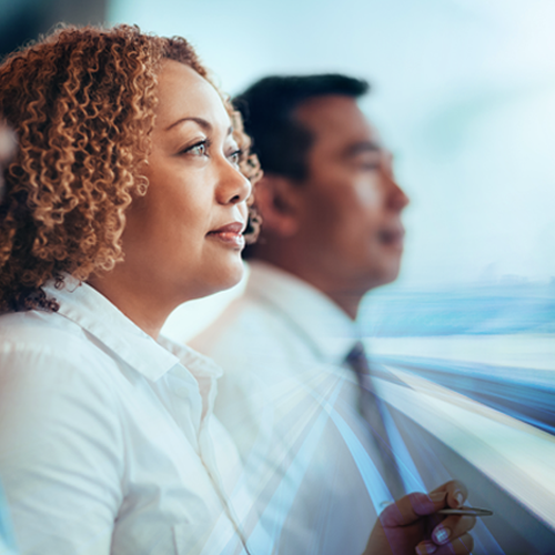 A woman with curly hair sits thoughtfully alongside two men, gazing forward as blurred motion suggests high-speed movement, conveying a sense of anticipation and focus in a dynamic environment.