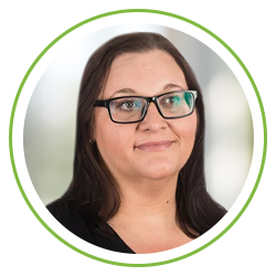 A woman with glasses and dark hair is smiling gently. She is positioned in a circular frame against a light, blurred background that suggests a professional setting.