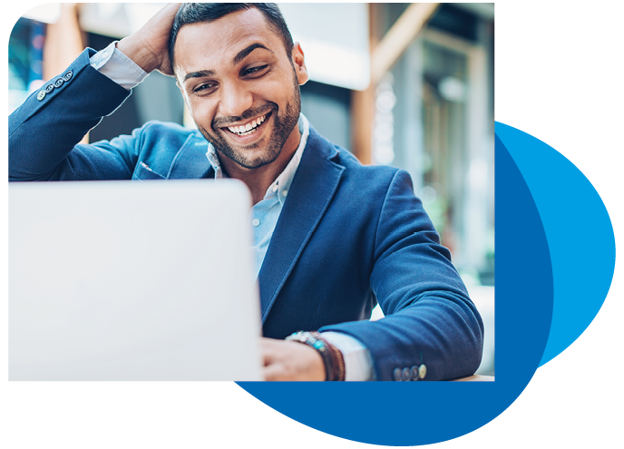 A man in a blazer smiles and interacts with a laptop, seated at a table in a well-lit, modern space. His hand is raised to his hair, suggesting engagement or amusement.