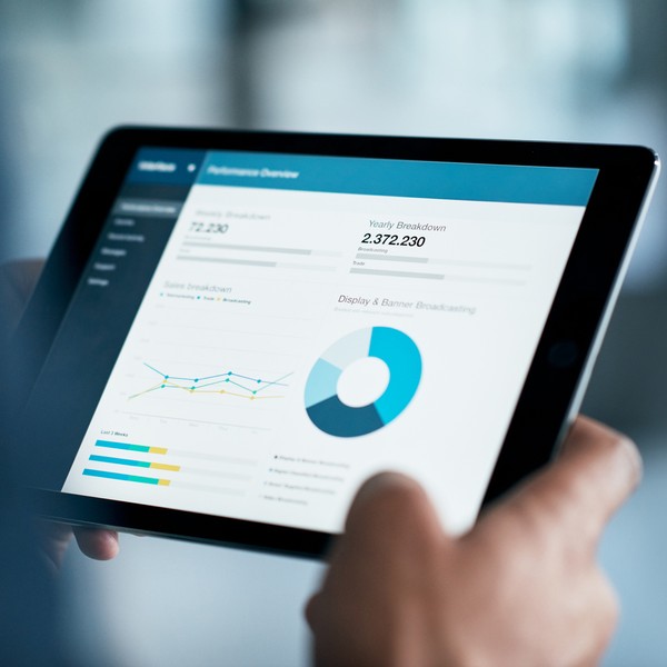 A person holds a tablet displaying a performance dashboard with graphs and data metrics. The context suggests a professional setting, likely focused on analyzing sales performance and trends.