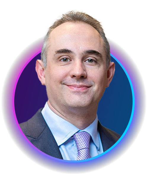 A man with short hair and a slight smile is centered in a circular frame. He is wearing a dark suit and a light blue shirt with a tie, against a colorful gradient background.