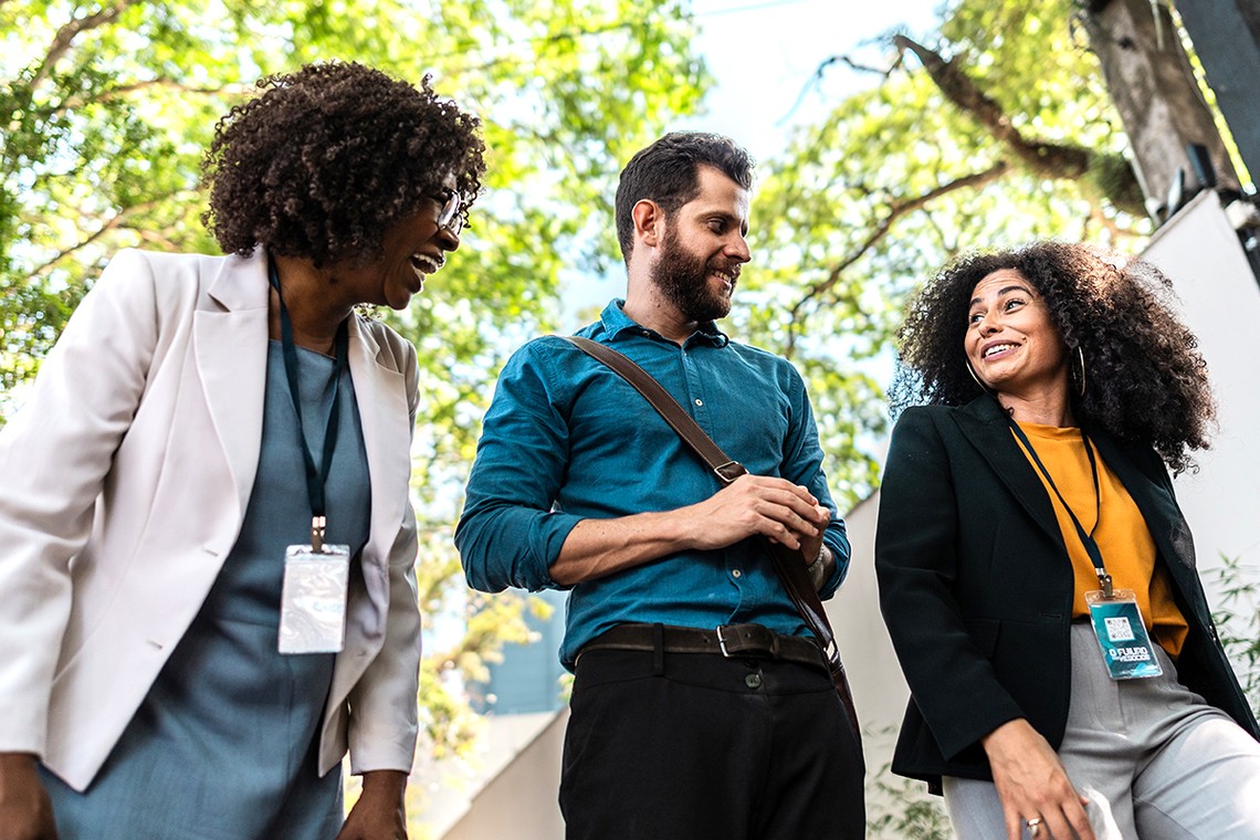 Three professionals with curly hair are engaged in a friendly conversation outdoors. They are surrounded by greenery, creating a vibrant and cheerful atmosphere.