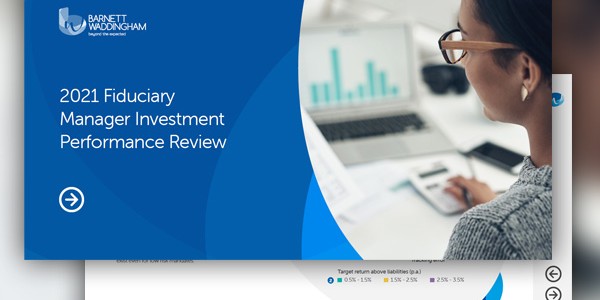 A presentation slide features a blue title box stating "2021 Fiduciary Manager Investment Performance Review." Behind it, a person observes financial charts on a laptop, focusing on data analysis.