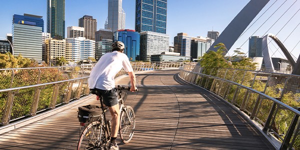 A cyclist rides on a curved wooden pathway, surrounded by modern skyscrapers under a clear blue sky, enjoying a bright day in an urban environment.