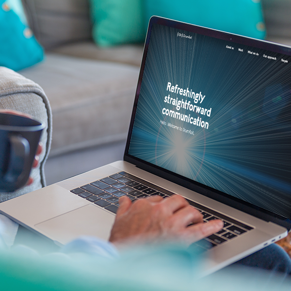 A laptop displays the text "Refreshingly straightforward communication. Hello. Welcome to blurt.ai." A person is typing on the keyboard, seated on a couch with teal cushions, holding a coffee mug.