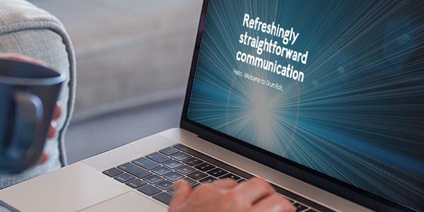 A laptop displays the text "Refreshingly straightforward communication. Hello. Welcome to blurt.ai." A person is typing on the keyboard, seated on a couch with teal cushions, holding a coffee mug.