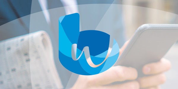 A person holds a smartphone while dressed in business attire, standing outdoors with a blurred background. A blue logo featuring stylized letters is prominently displayed in the foreground.