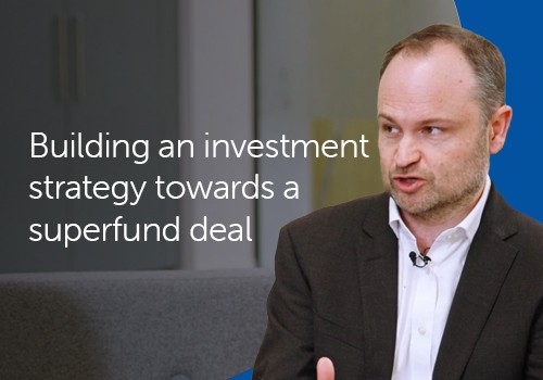 A man in a dark blazer is speaking, focused on discussing an investment strategy, while seated against a soft background with muted colors. Text includes: "Building an investment strategy towards a superfund deal."