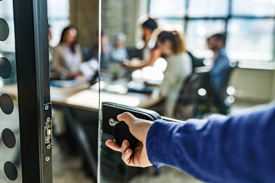A person unlocking access to a room filled with investment professionals during a meeting