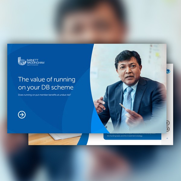 A professional man in a suit gestures while discussing an investment topic related to defined benefit schemes. The background features presentation material with text about member benefits and risks.