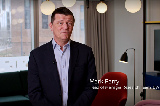 A man in a blazer stands and speaks, expressing thoughts in a modern office setting with couches and pendant lights in the background. Text: "Mark Parry, Head of Manager Research Team, BW."